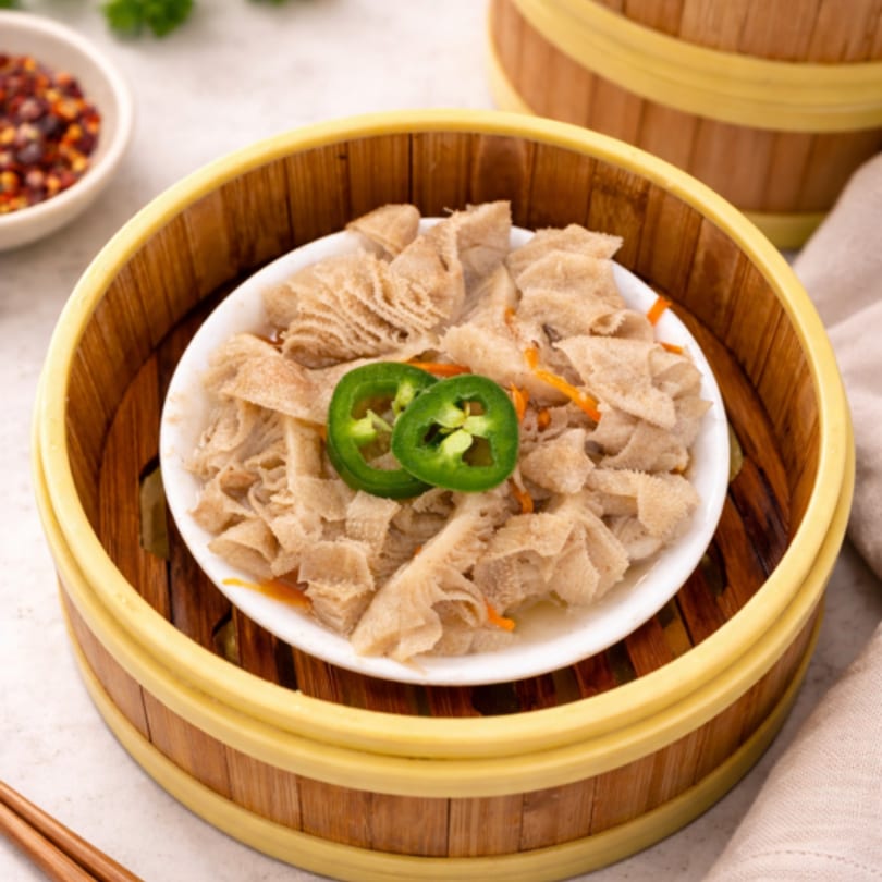 Steamed tripe with sliced green chilies and carrots in a white bowl inside a bamboo steamer.