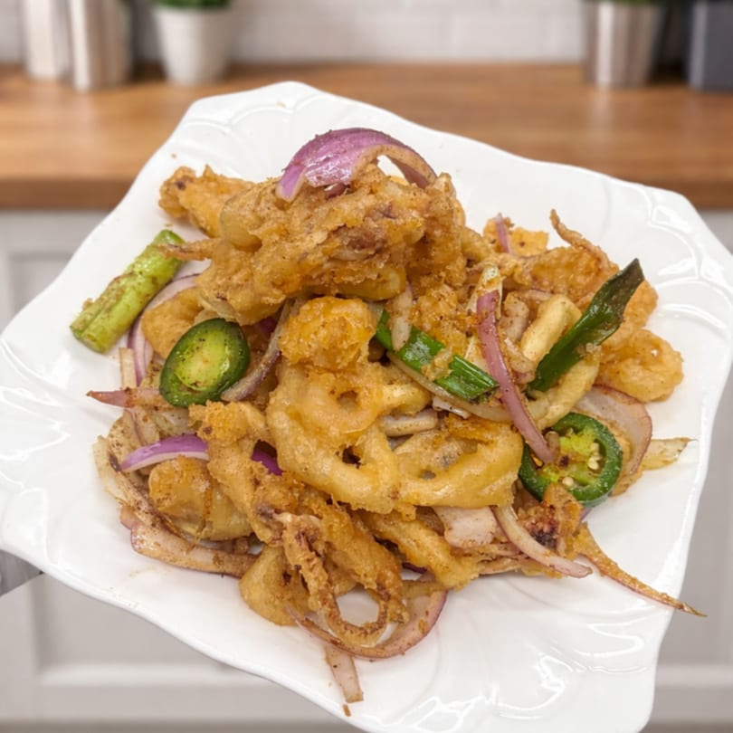 Crispy fried calamari with red onions, green onions, and sliced jalapeños on a white plate.